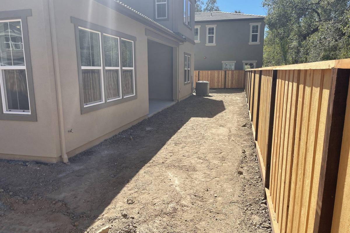 Before: the same side of the house with bare, graded soil beside a new wood fence